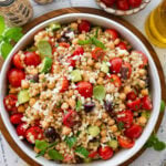Pearl couscous salad in a serving bowl with a spoon and more ingredients nearby.