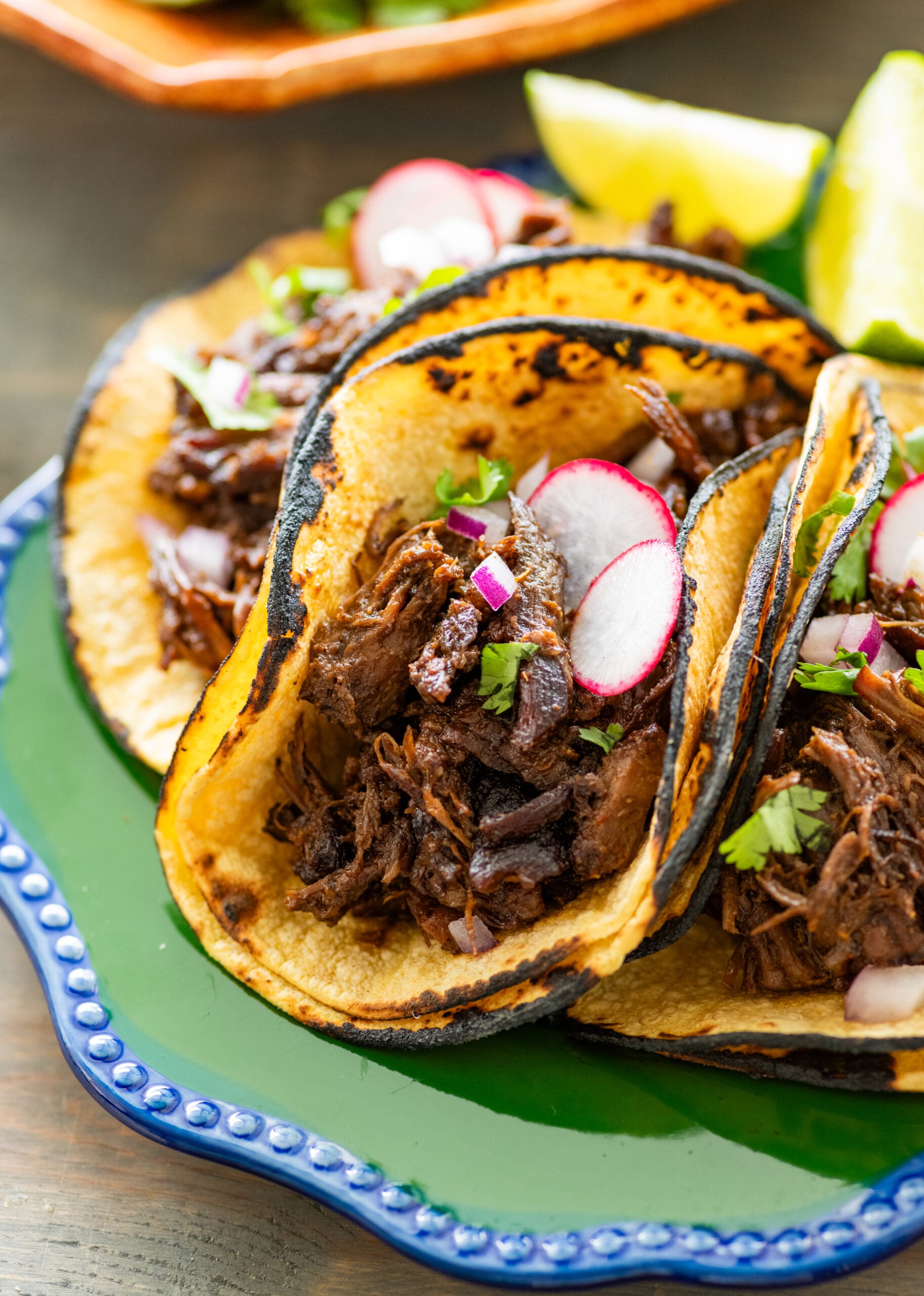 Barbacoa beef in three taco shells, with more toppings.
