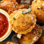 A plate of fried ravioli with garnish and a bowl of marinara sauce.