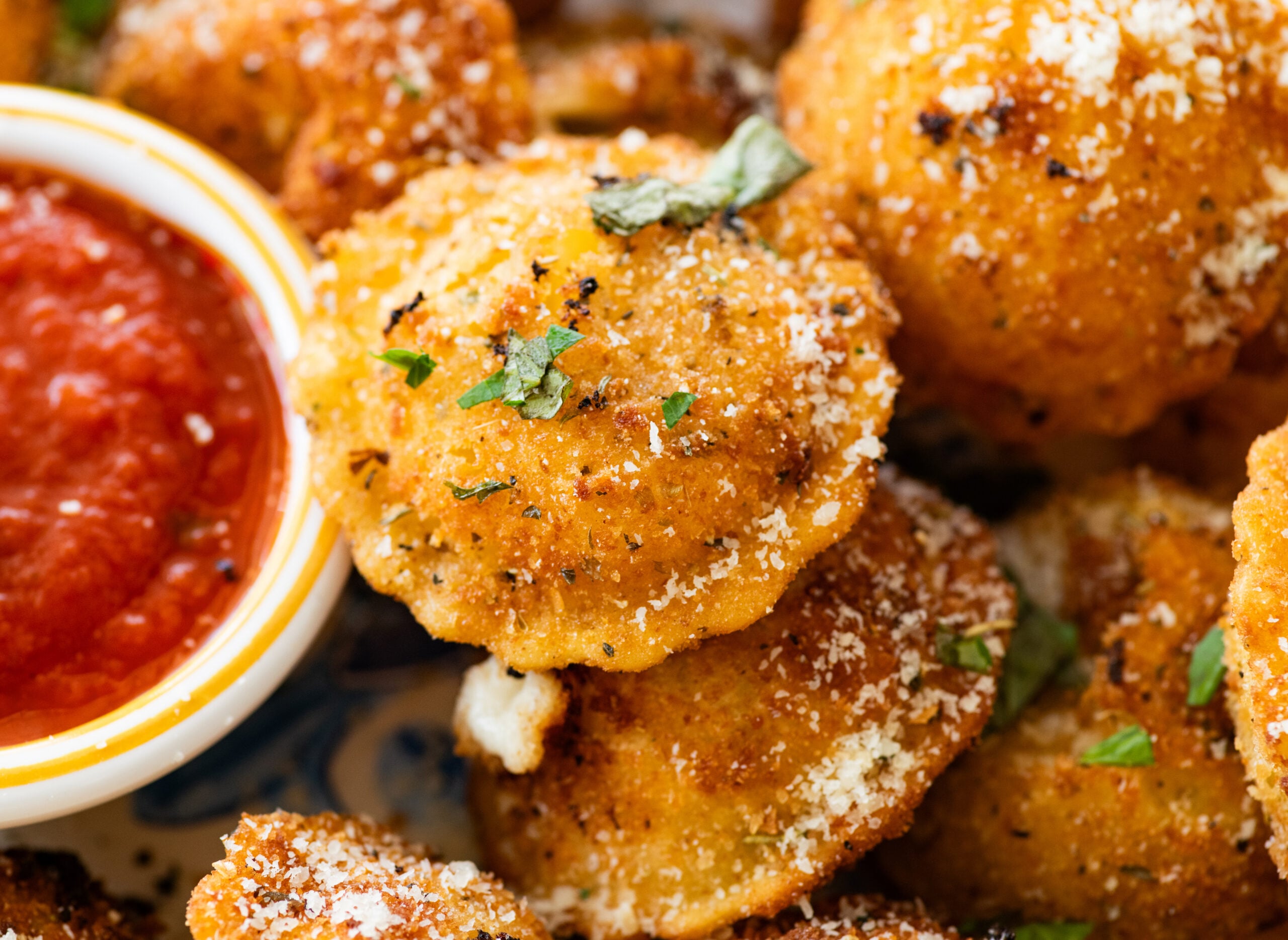 A plate of fried ravioli with garnish and a bowl of marinara sauce.
