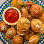 A plate of fried ravioli with garnish and a bowl of marinara sauce.