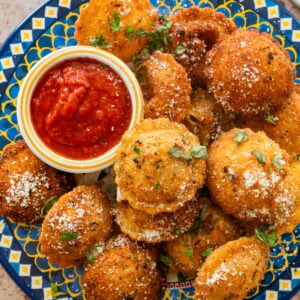 A plate of fried ravioli with garnish and a bowl of marinara sauce.