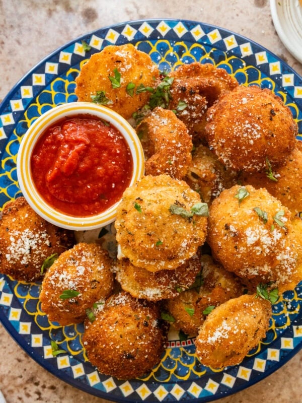 A plate of fried ravioli with garnish and a bowl of marinara sauce.
