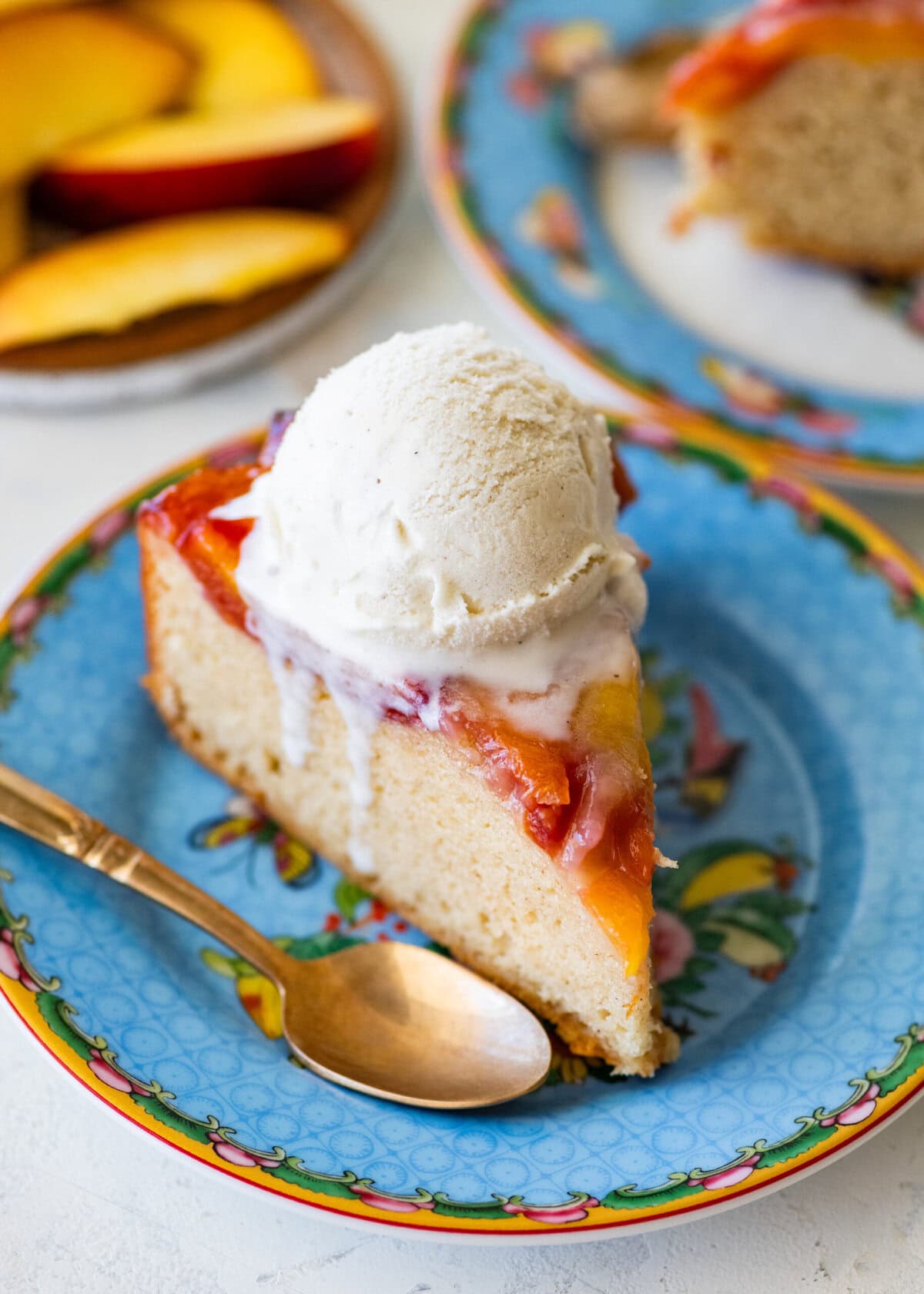 A slice of cake on a plate with a scoop of ice cream on top, a spoon resting on the edge, and more ingredients nearby.