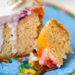 A slice of cake topped with ice cream resting on a plate with a spoon taking one bite out,