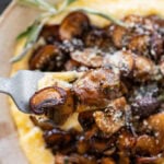 A bowl of polenta topped with mushrooms and garnish, with a spoon holding up one bite.