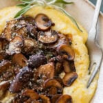 A bowl of polenta topped with mushrooms and garnish, with a spoon resting inside.