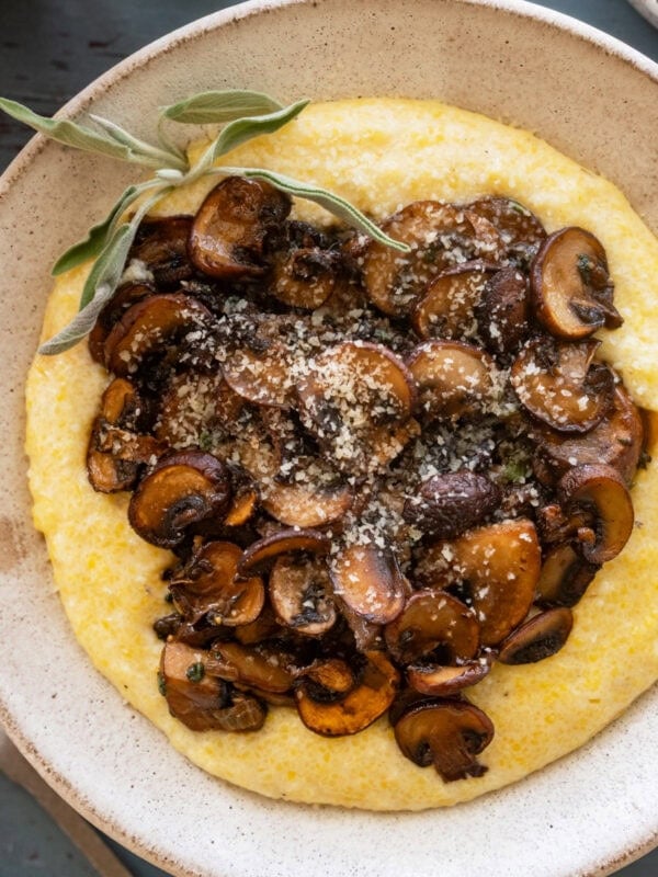 A bowl of polenta topped with mushrooms and garnish, with more ingredients nearby.