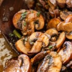 Cooked mushrooms in a large pot with a wooden spoon resting inside.