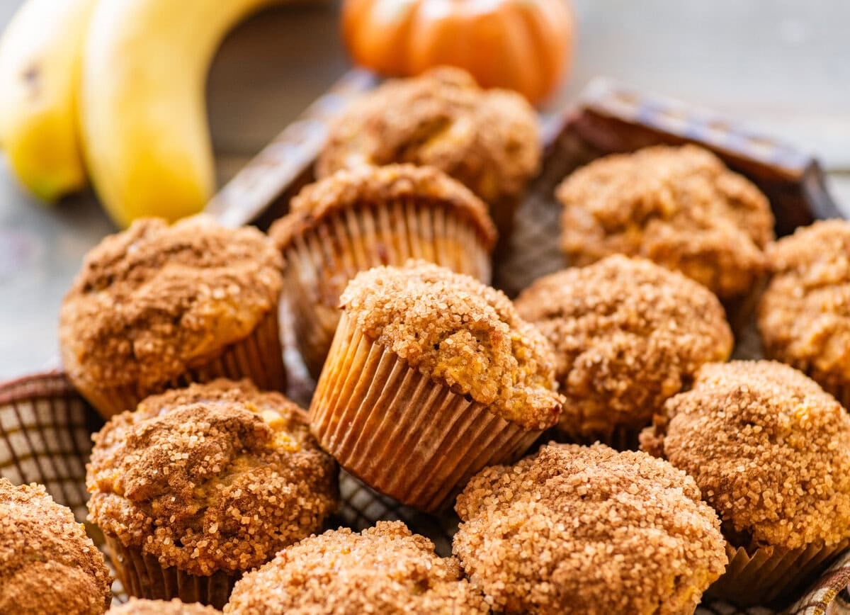A tray of pumpkin banana muffins with bananas and pumpkins nearby.