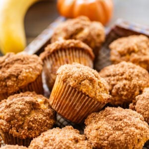 A tray of pumpkin banana muffins with bananas and pumpkins nearby.