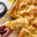 a hand holding up a slice of bread over the baking dish of braed.