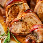 Bacon wrapped pork tenderloin on a plate cut into medallions.