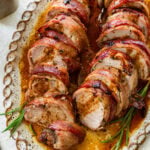 Bacon wrapped pork tenderloin on a plate cut into medallions.