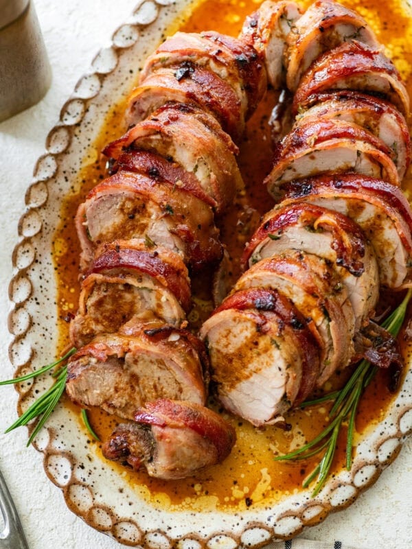 Bacon wrapped pork tenderloin on a plate cut into medallions.