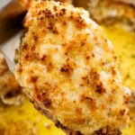 a parmesan crusted chicken breast being held with a utensil over a pan after baking and broiling.