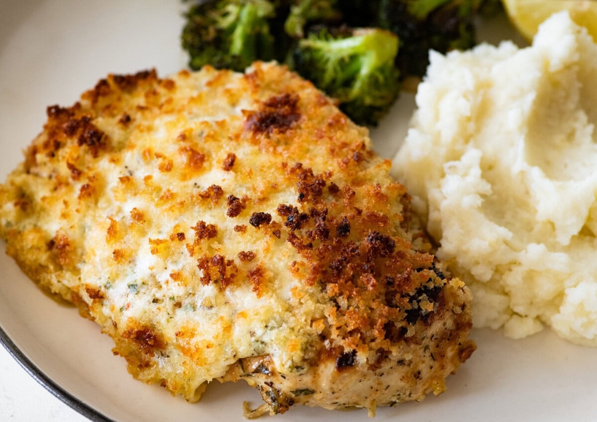 a chicken breast on a plate served with broccoli and mashed potatoes.