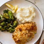 a chicken breast on a plate served with broccoli and mashed potatoes
