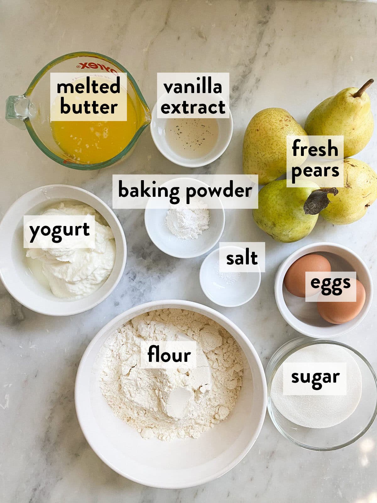 bowls of ingredients for pear cake on a marble countertop.