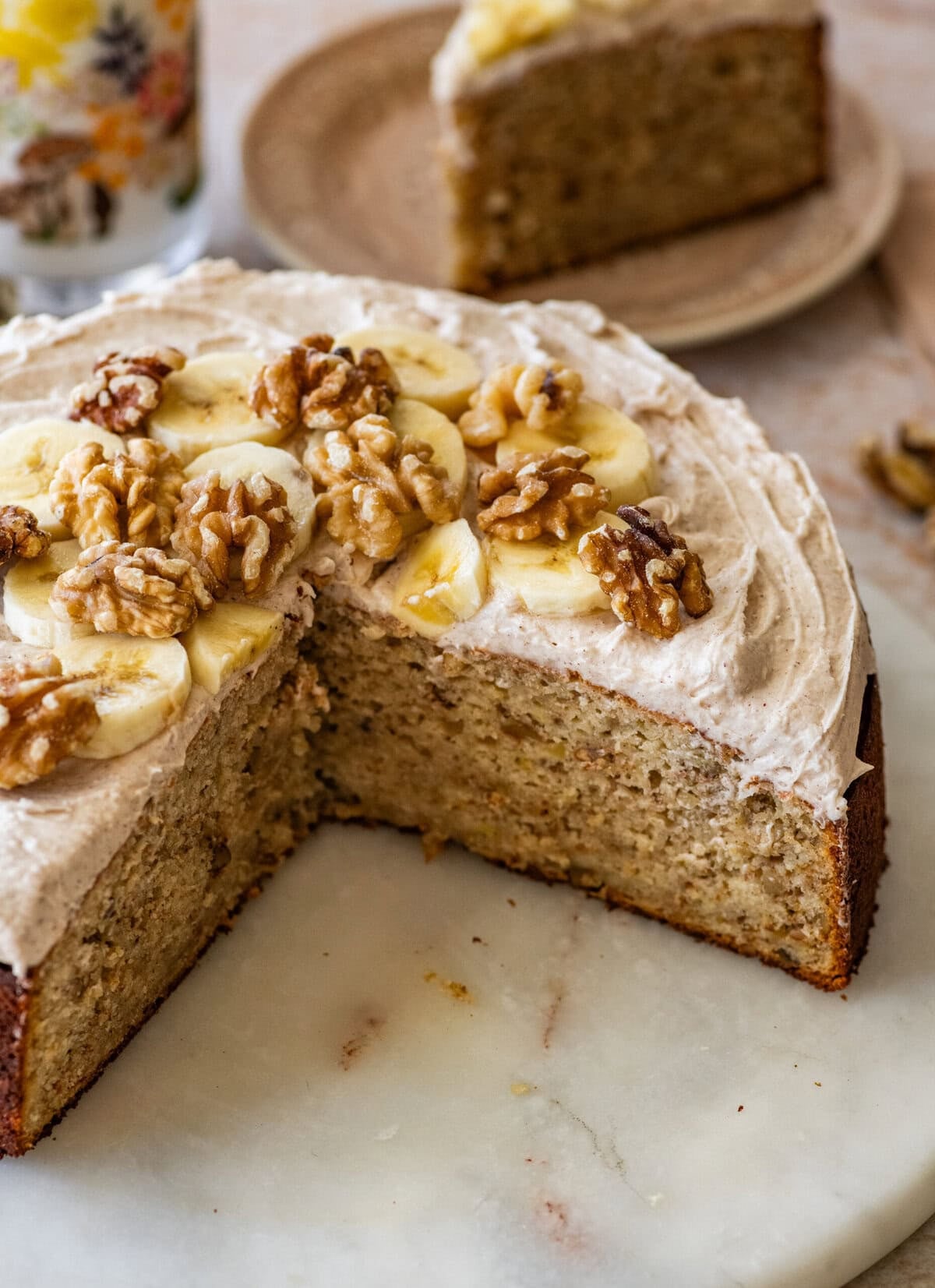 Frosted banana nut cake garnished with nuts and banana slices, with a slice removed.