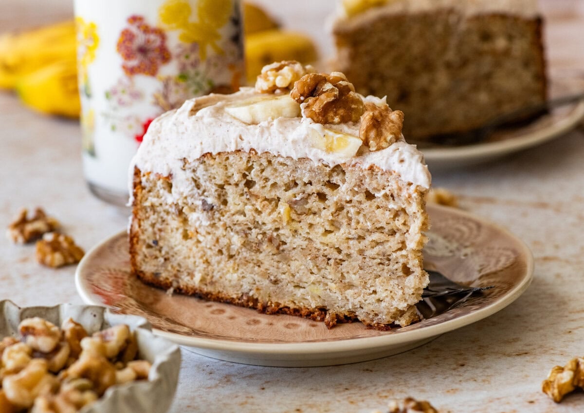 A slice of banana nut cake garnished with banana slices and nuts, with more ingredients nearby.
