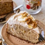 A slice of banana nut cake garnished with banana slices and nuts, with more ingredients nearby.