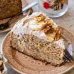 A slice of banana nut cake garnished with banana slices and nuts, with more ingredients nearby.