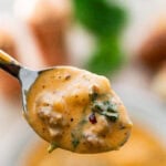 A bowl of sausage gnocchi soup with a spoon lifting some and more ingredients nearby.