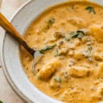 A bowl of sausage gnocchi soup with a spoon resting inside.