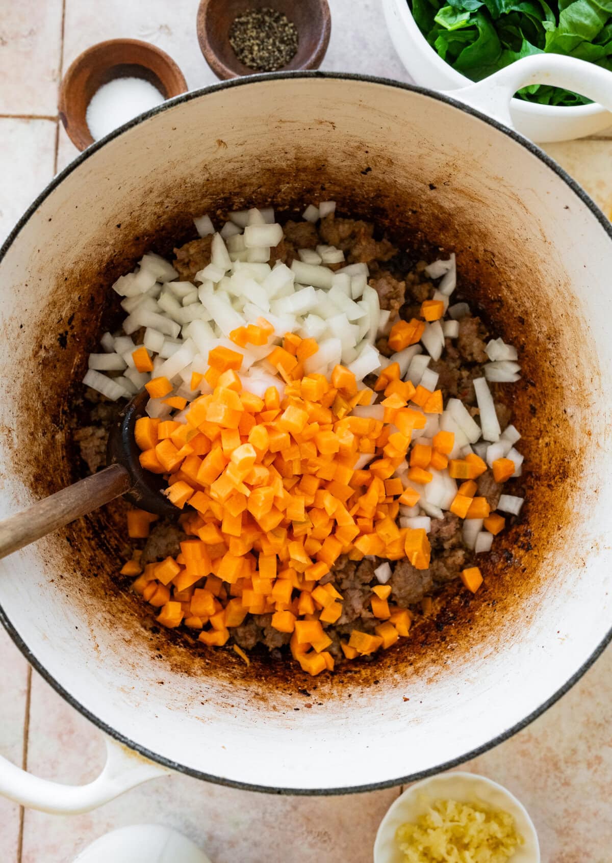 Vegetables added to a large soup pot with a spoon stirring them.