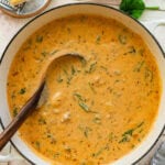 A pot of sausage gnocchi soup with more ingredients nearby and a spoon resting inside.