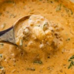 A pot of sausage gnocchi soup with more ingredients nearby and a spoon holding up some.