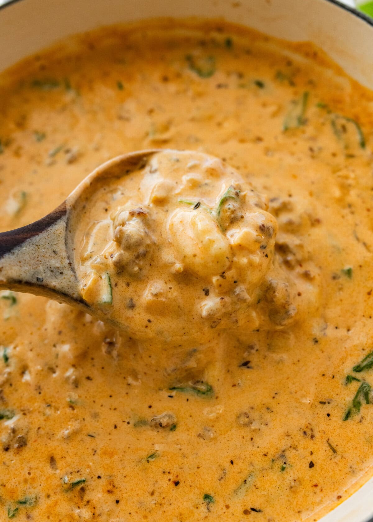 A pot of sausage gnocchi soup with more ingredients nearby and a spoon holding up some.