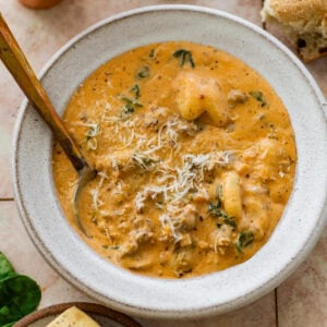 A bowl of sausage gnocchi soup with a spoon resting inside.