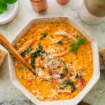 A bowl of tuscan chicken soup with more ingredients nearby and a spoon inside the bowl.