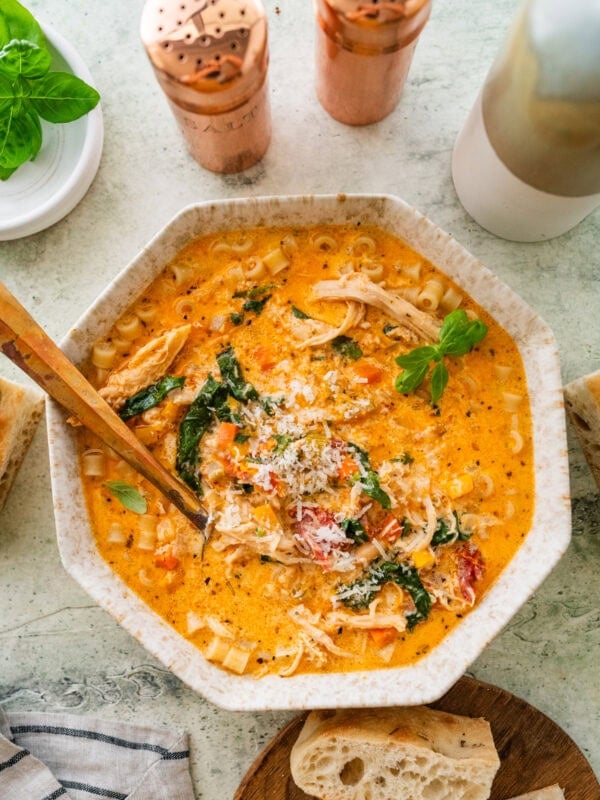 A bowl of tuscan chicken soup with more ingredients nearby and a spoon inside the bowl.