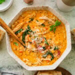 A bowl of tuscan chicken soup with more ingredients nearby and a spoon inside the bowl.