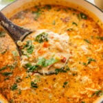 A pot of tuscan chicken soup with more ingredients nearby and a spoon holding some up.