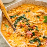 A bowl of tuscan chicken soup with more ingredients nearby and a spoon inside the pot.
