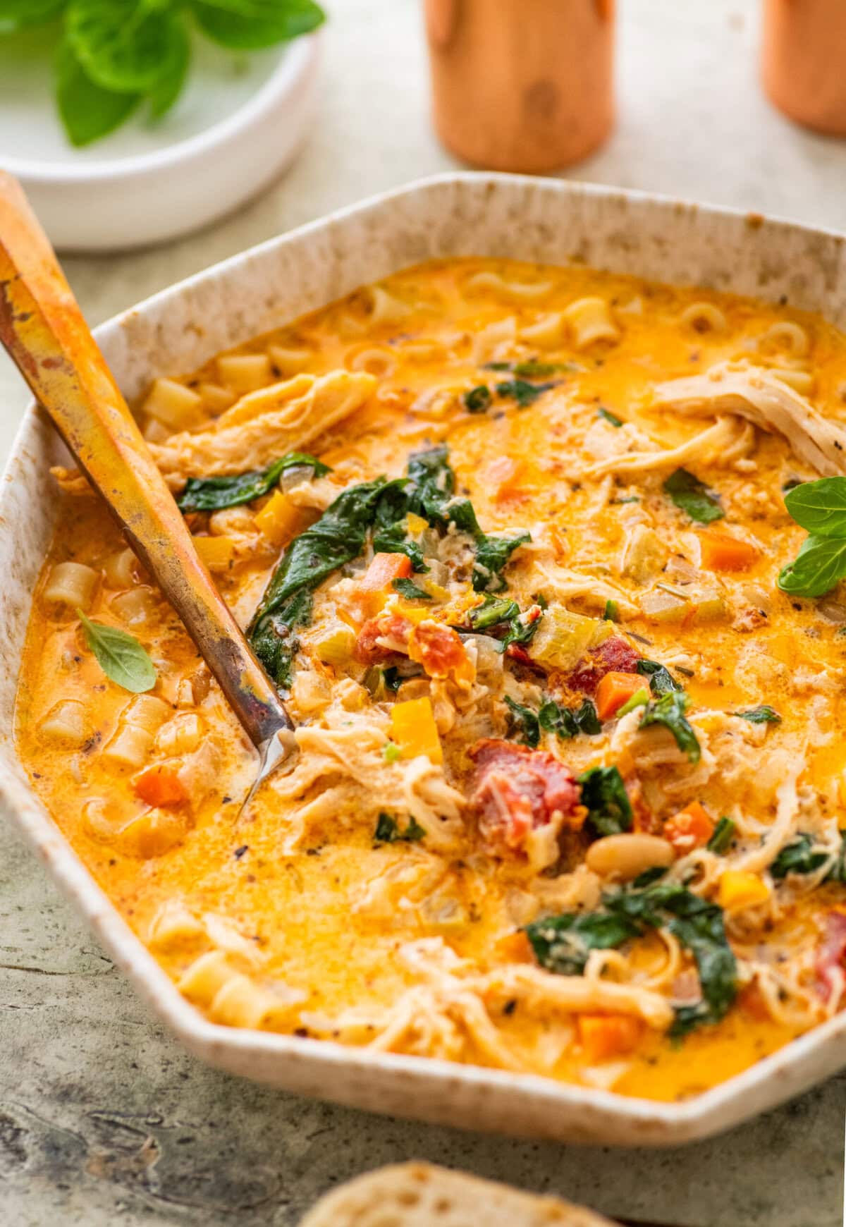 A bowl of tuscan chicken soup with more ingredients nearby and a spoon inside the pot.