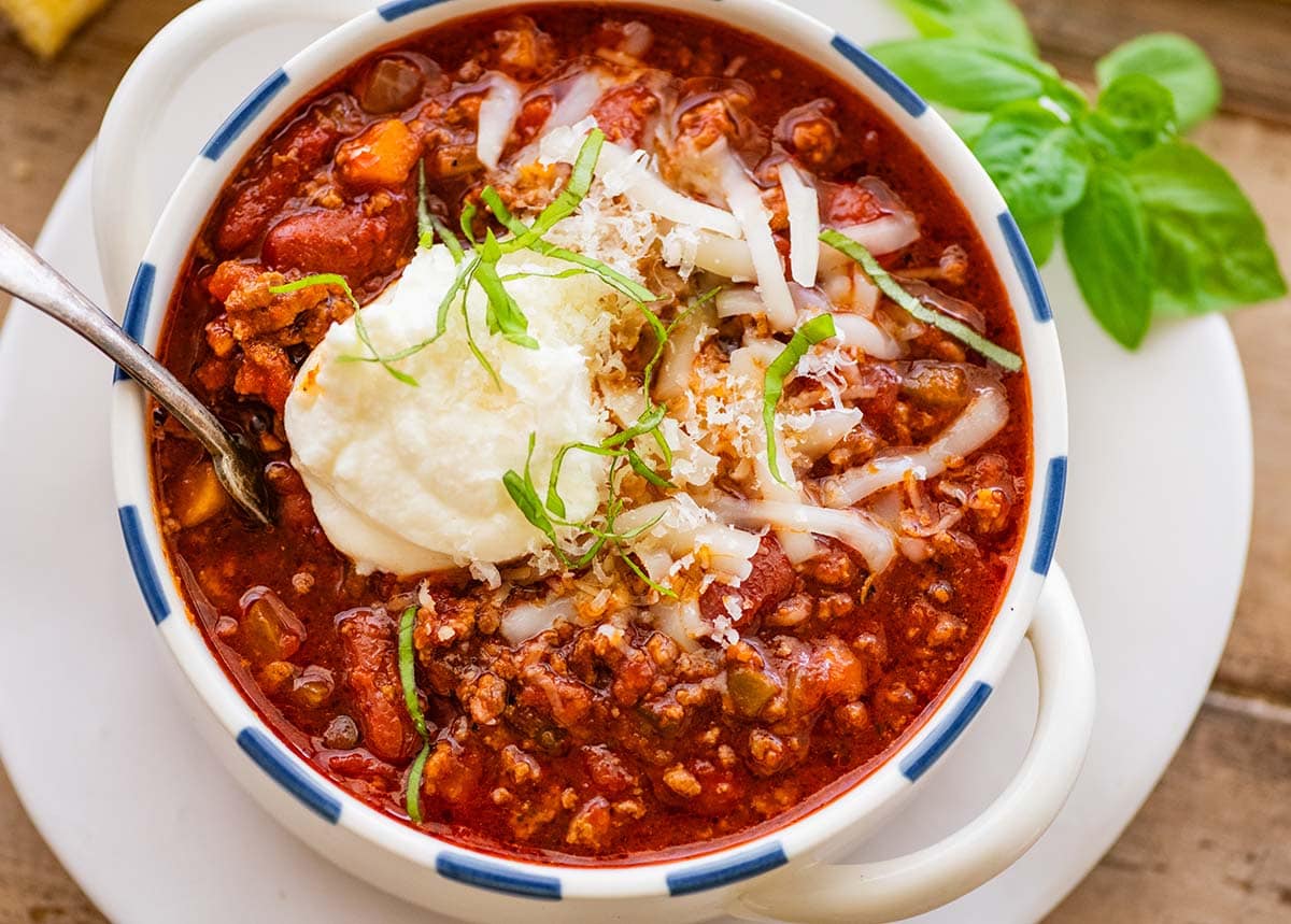 bowl of beef and bean chili garnished with cheese and basil ribbons.