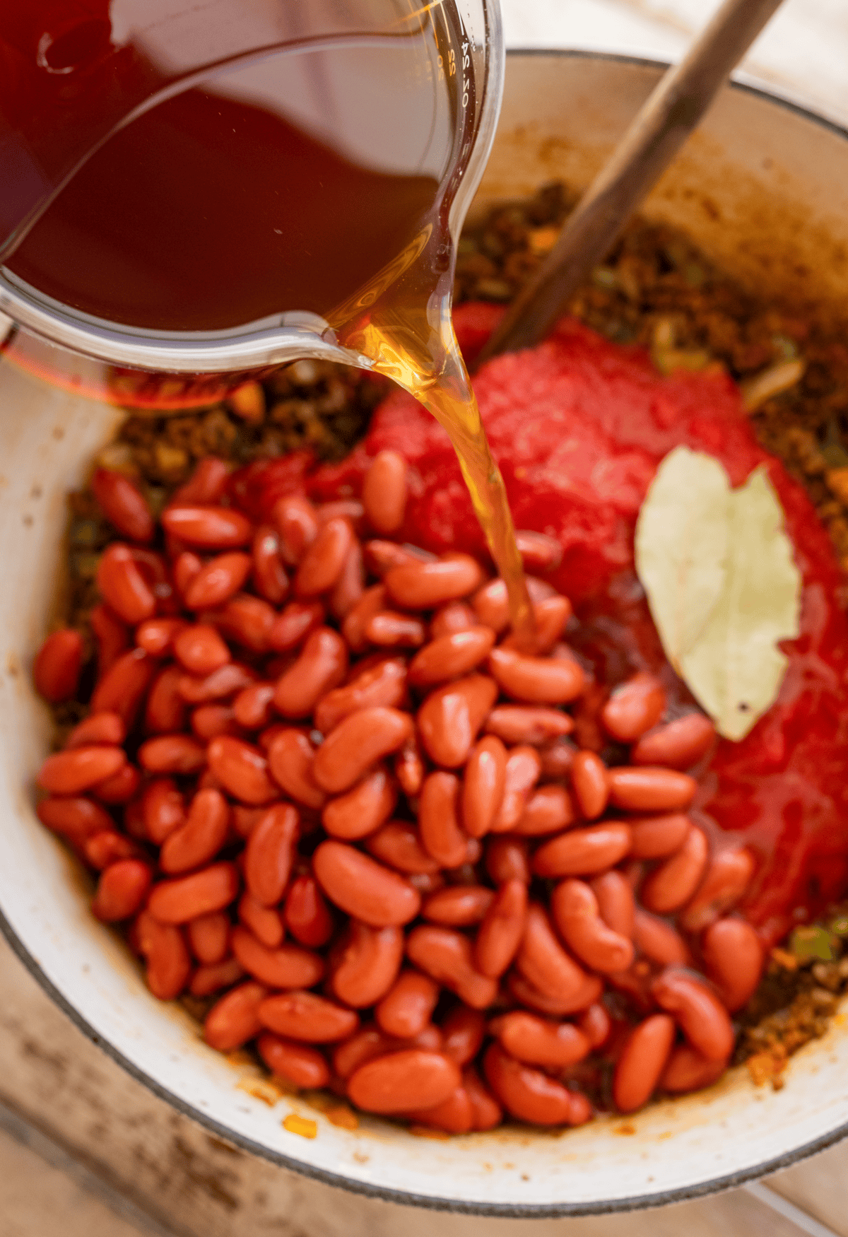 adding the beef broth and beans to the chili base.