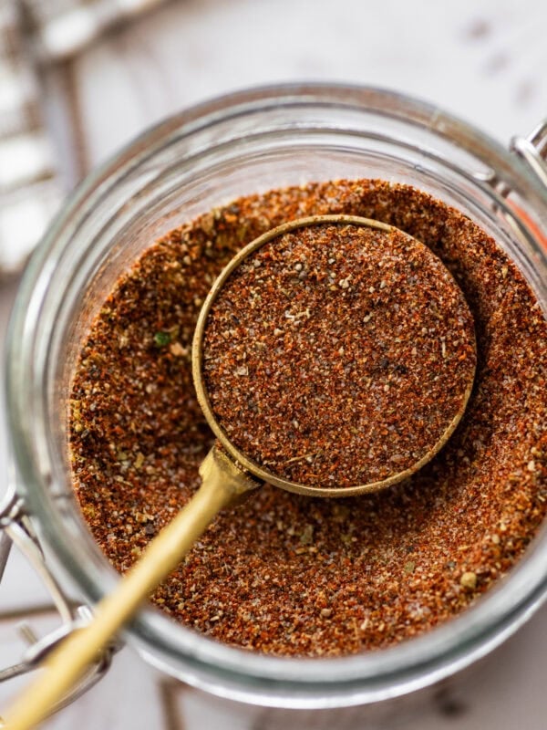 A scoop of seasoning held over a jar with more.