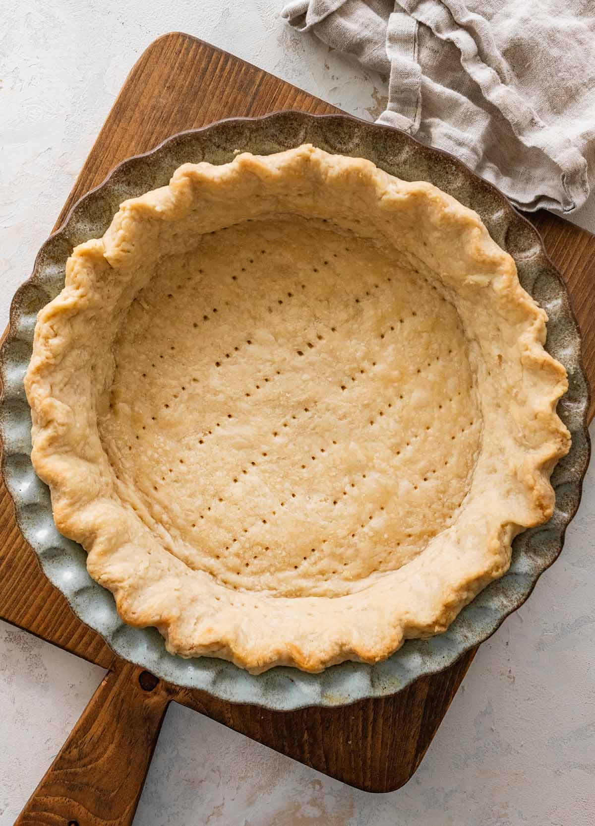 baked Crisco pie crust in a ceramic pie crust on a wooden cutting board.