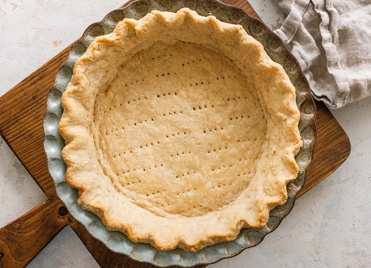 Classic Crisco Pie Crust Recipe (flaky) baked Crisco pie crust in a ceramic pie crust on a wooden cutting board.