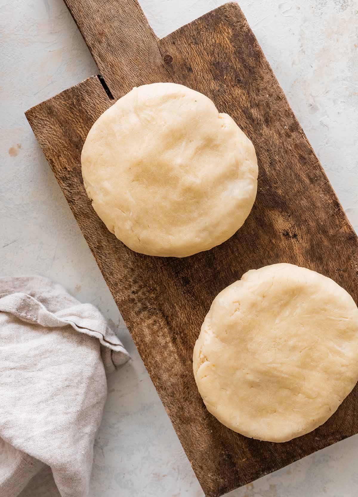 Classic Crisco Pie Crust Recipe two disks of pastry on a wooden cutting board.