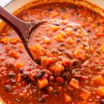 A ladel holding up a scoop of chili over the pot.